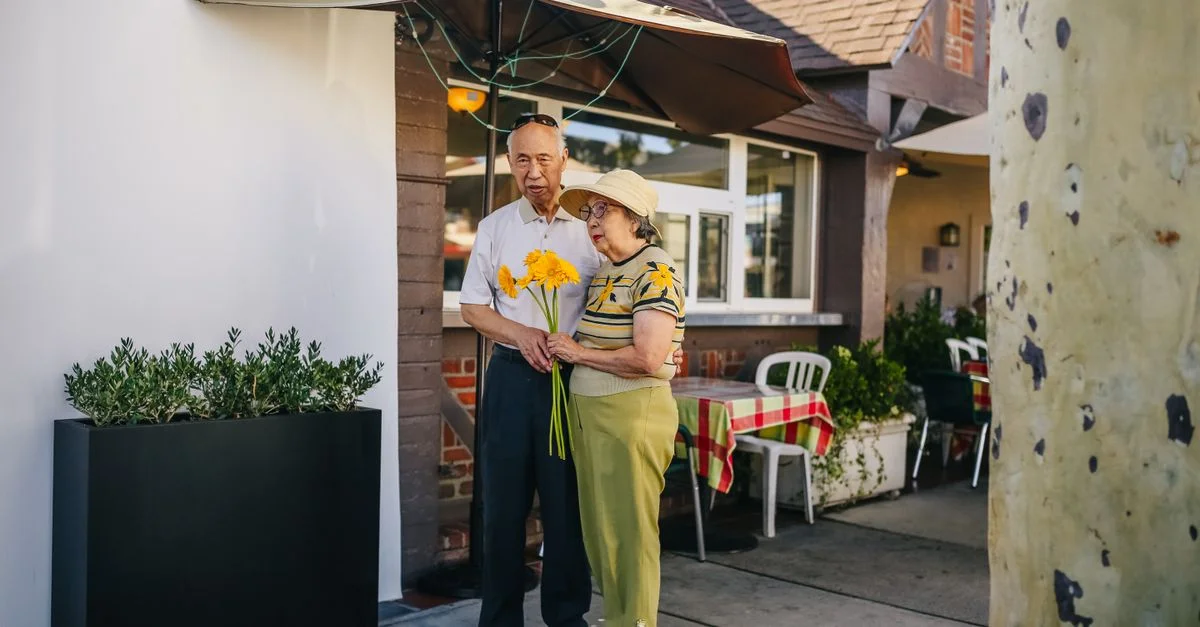 Un couple senior partageant une affection sincère avec un cadeau de tournesols en plein air.