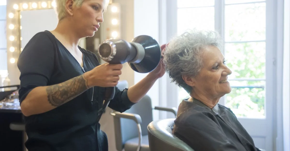 Un coiffeur expérimenté sèche les cheveux d'une femme senior dans un salon moderne.