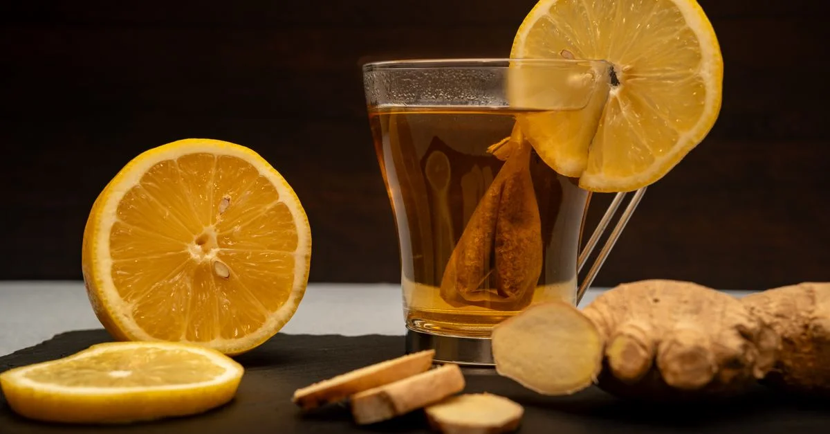 Une tasse chaude de thé au citron et au gingembre entourée de tranches de citron frais et de racine de gingembre sur de l'ardoise.