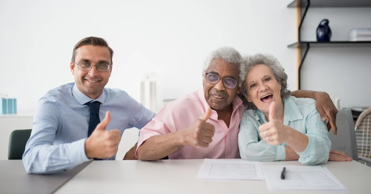 Couple âgé avec un consultant faisant un pouce levé dans un cadre de bureau, montrant une interaction positive.