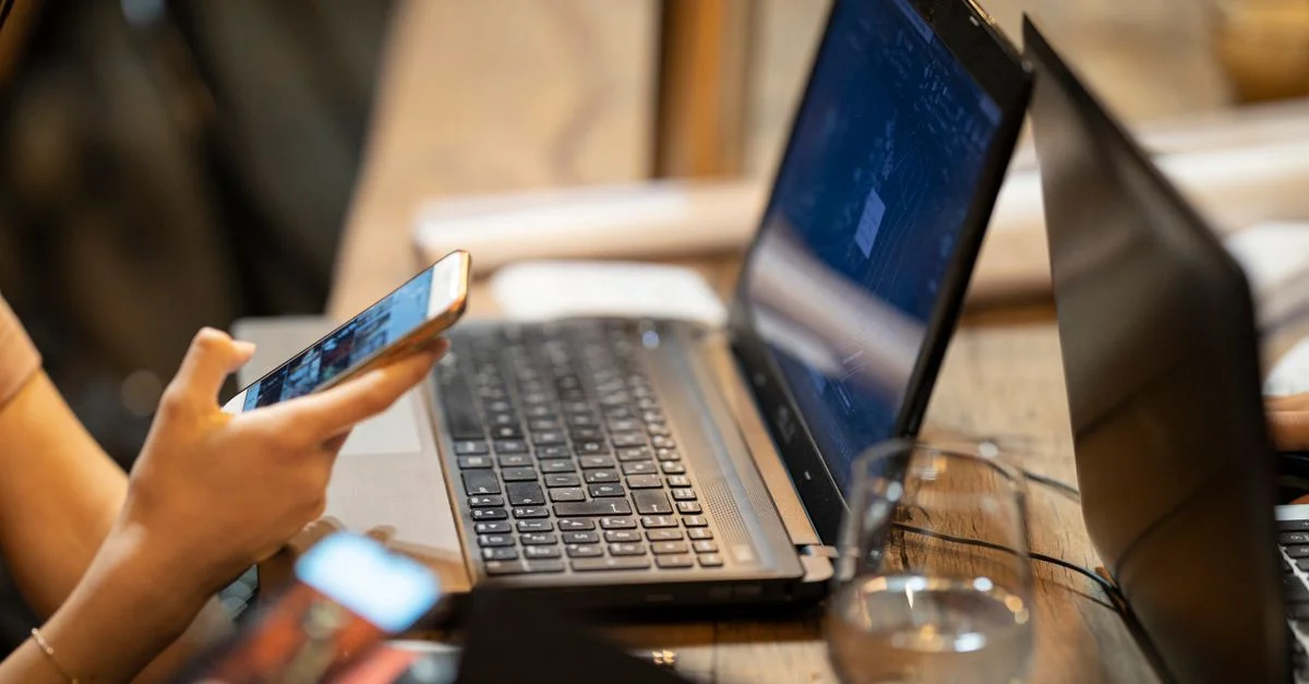 Personne utilisant un smartphone et un ordinateur portable dans un environnement de travail intérieur confortable.