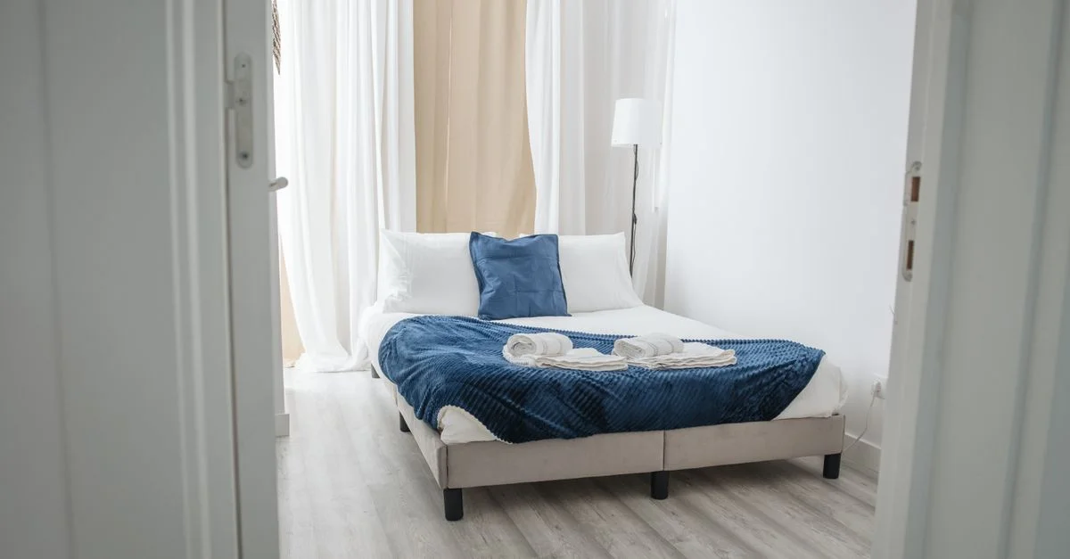 Chambre lumineuse et minimaliste avec un plaid bleu et des coussins, idéale pour la détente.
