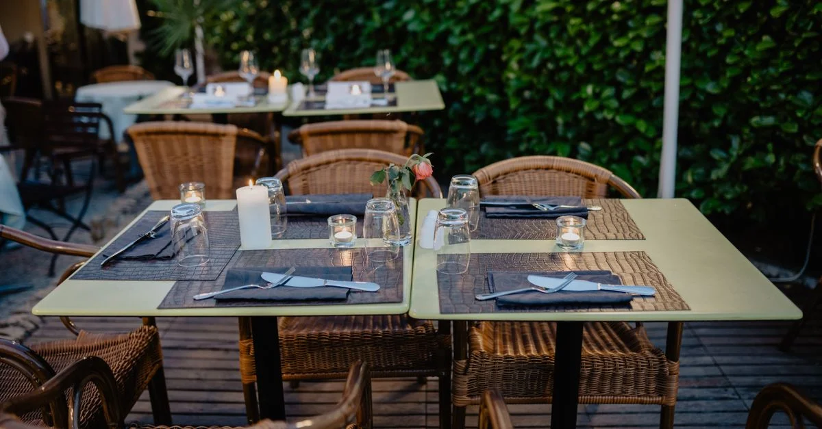 Cadre de repas intime en plein air avec des chaises en rotin et des tables éclairées aux bougies sur une terrasse charmante.