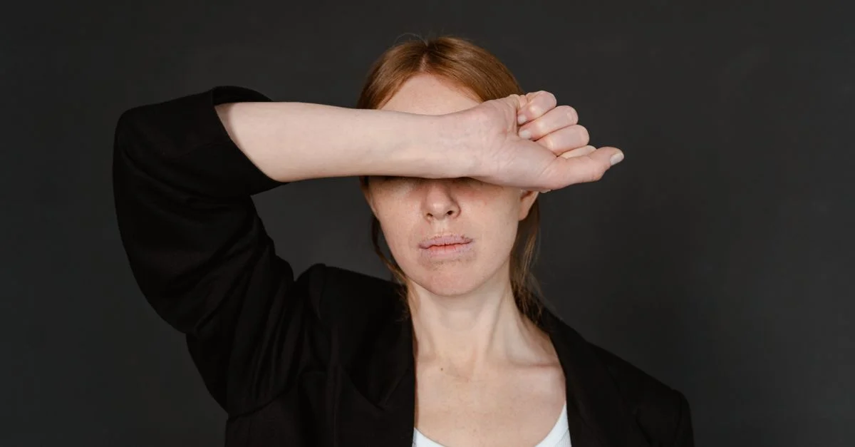 Gros plan sur une femme en blazer noir se couvrant les yeux avec son bras.