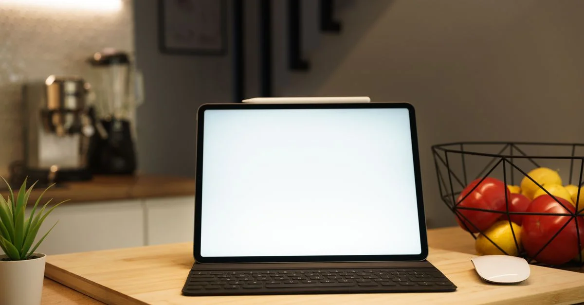 Un espace de travail de cuisine moderne comprenant une tablette avec clavier, souris et bol de fruits sur une table en bois.