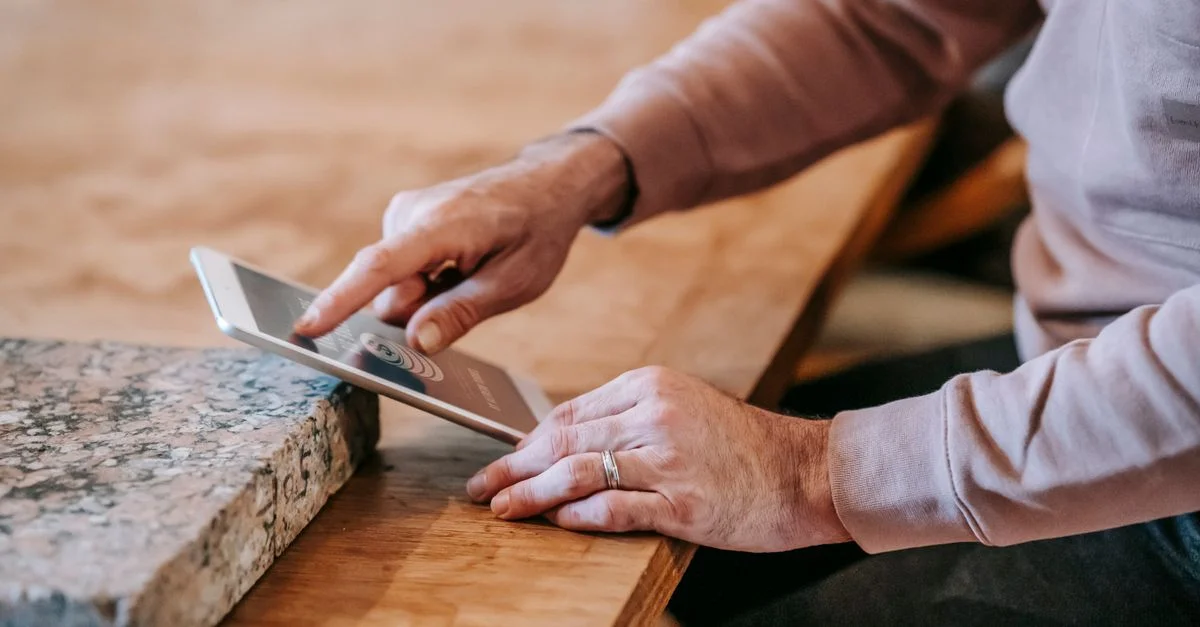 Gros plan des mains d'un homme utilisant une tablette sur une table en bois à l'intérieur.