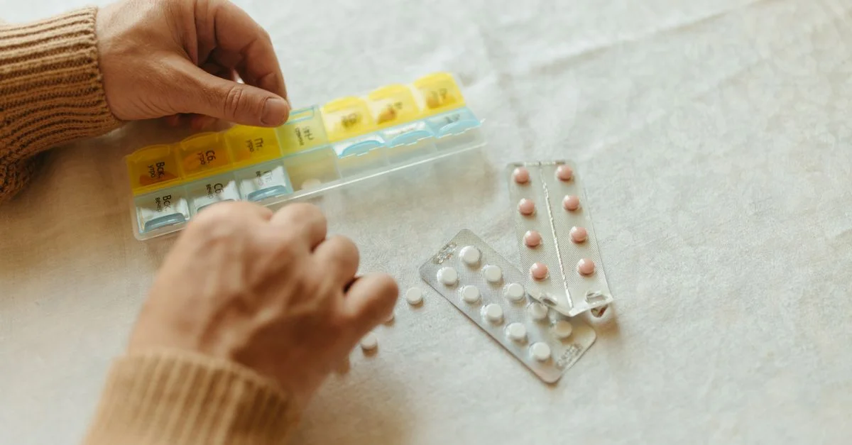 Gros plan sur des mains organisant des comprimés dans un pilulier hebdomadaire pour la gestion quotidienne des médicaments.