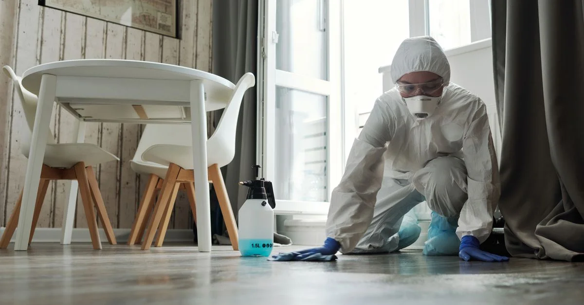 Personne de nettoyage spécialisée en costume de protection désinfectant un sol à l'intérieur pour l'hygiène et la sécurité.