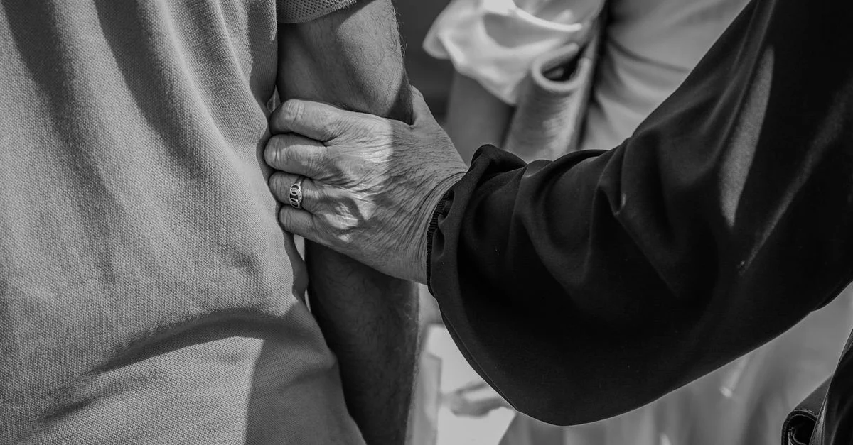 Photo en noir et blanc d'un couple de personnes âgées se tenant par le bras, symbolisant le soutien et l'attention.