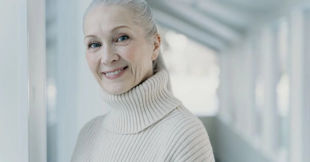 Femme senior élégante avec des cheveux gris souriante dans un cadre intérieur serein.