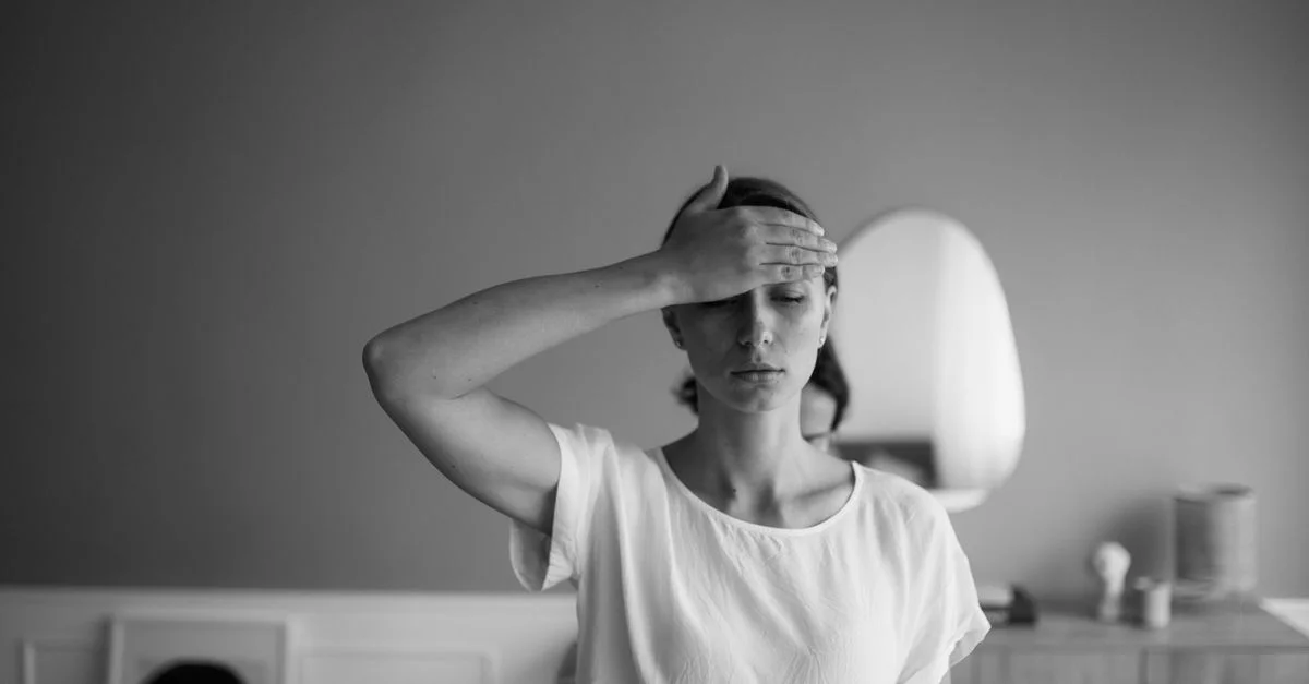 Image en noir et blanc d'une femme avec la main sur le front, les yeux fermés et sereine.
