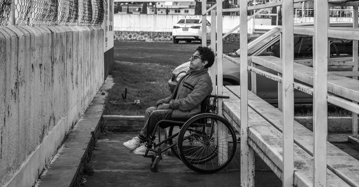 Photo en noir et blanc d'un homme en fauteuil roulant près des gradins d'un stade à Atlacomulco, au Mexique.