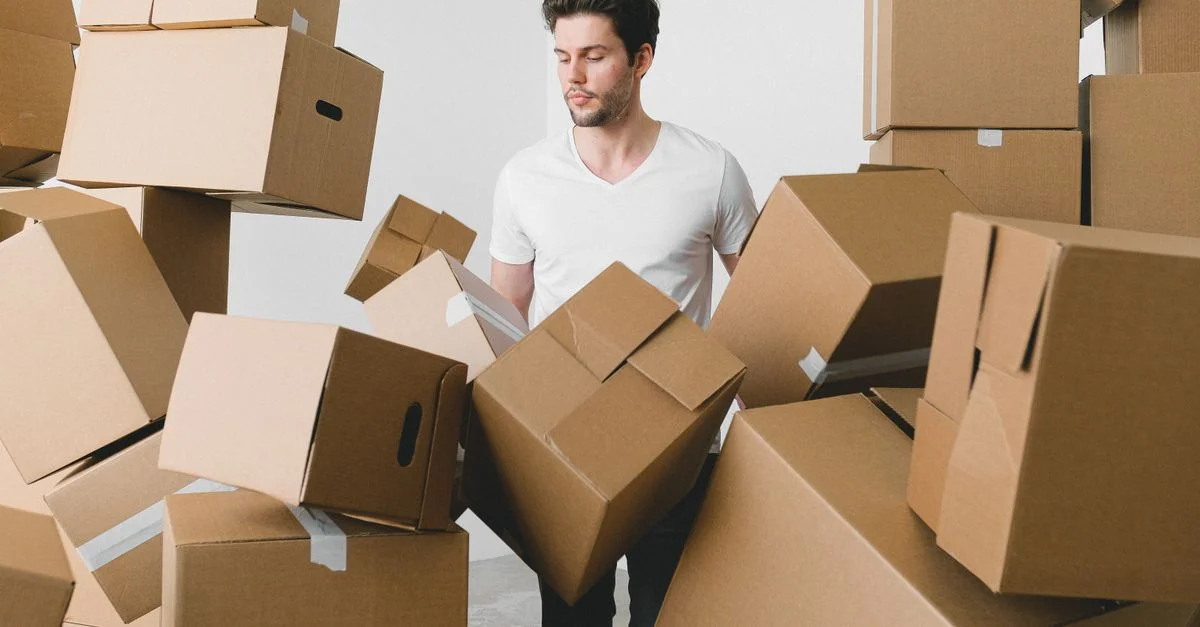 Un jeune homme entouré de boîtes de déménagement à l'intérieur, contemplant le déballage.
