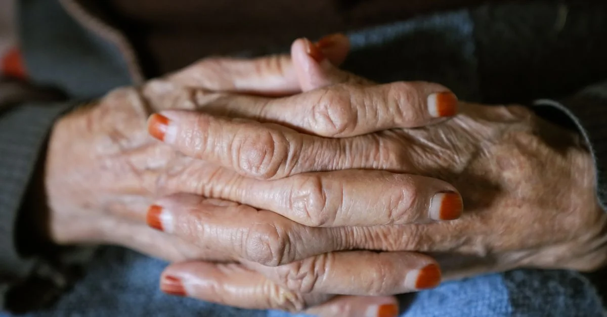 Vue détaillée des mains d'un adulte âgé avec des ongles peints croisés doucement, transmettant chaleur et sagesse.