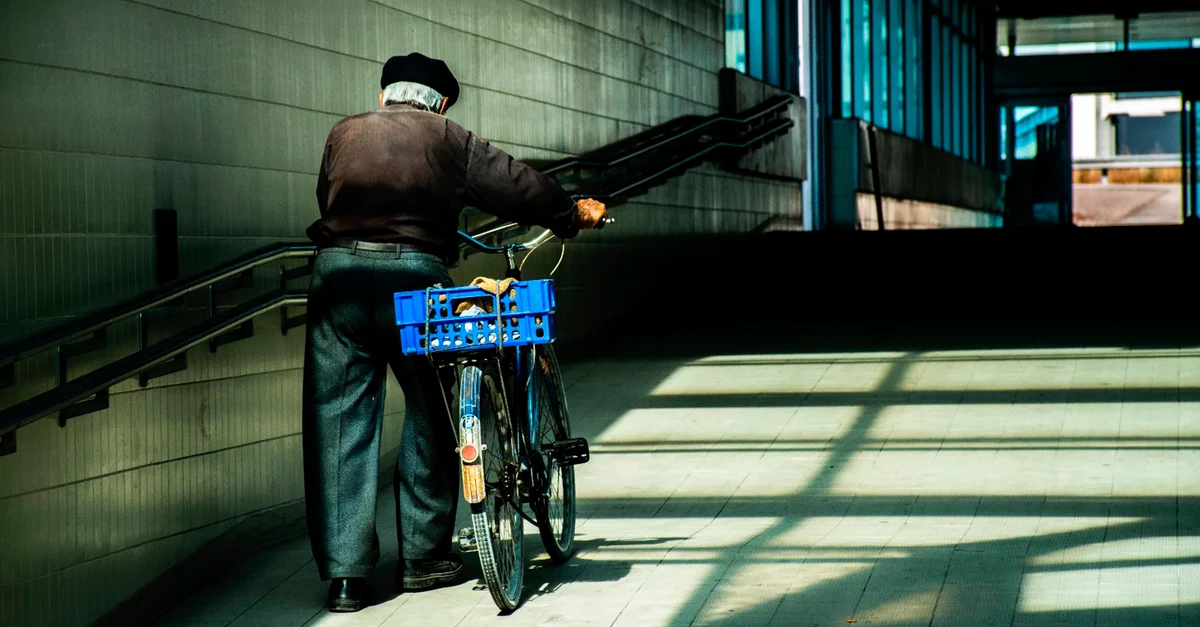 Homme senior marchant avec un vélo dans un couloir intérieur carrelé à Pinhal Novo, Portugal.